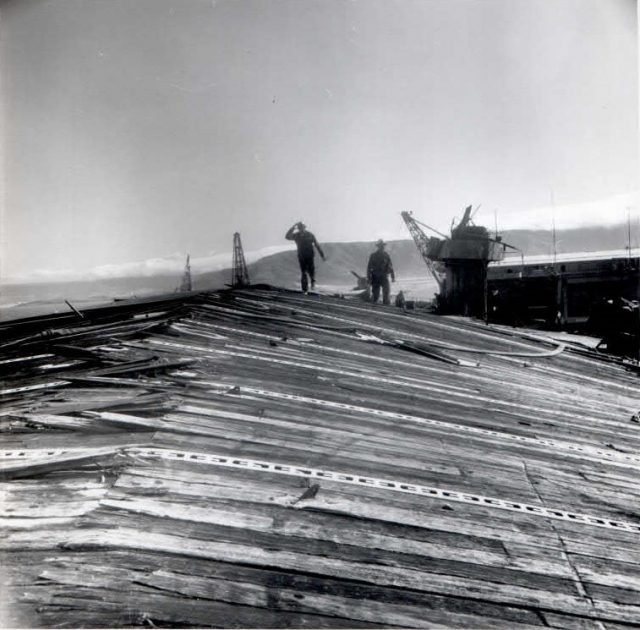 CVL-22 flight deck damage from the "Able" blast (as described above). The ships island and crane are behind and on the right side of the worker. (Photo: Scan by John G. Lambert at NARA San Bruno, CA on the 2015 Independence mission.)